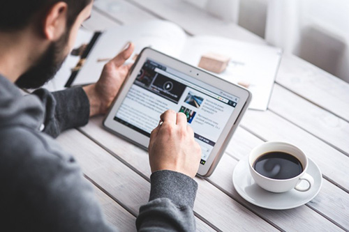 A man swiping on an iPad with a cup of coffee next to him